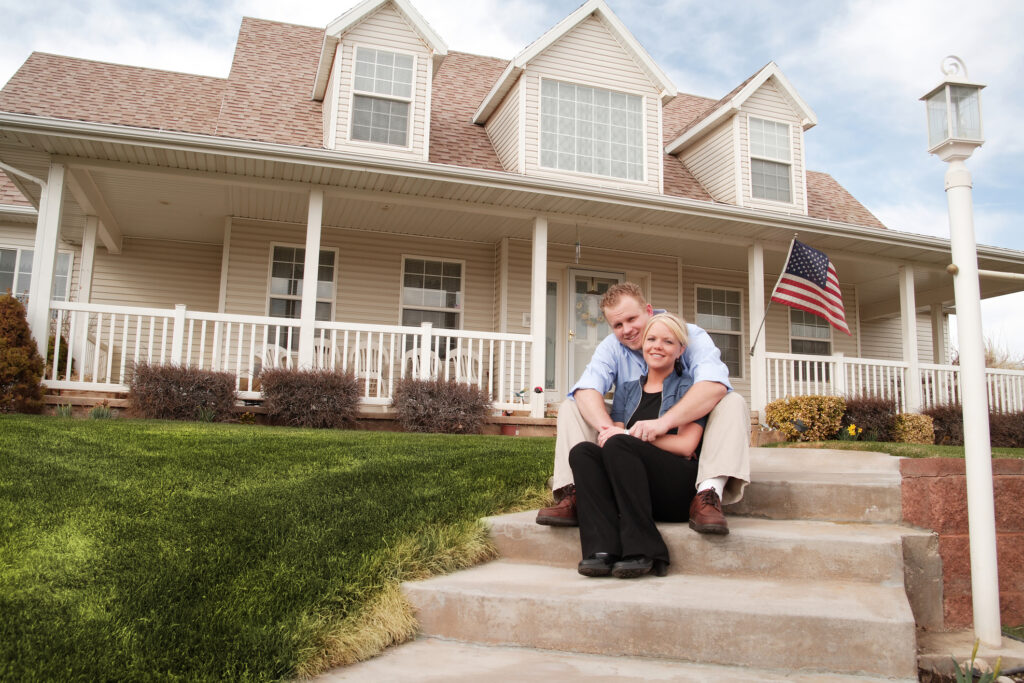 Veteran couple sitting on the front steps of their home with an American flag, representing VA 100% P&T benefits for veterans and their families