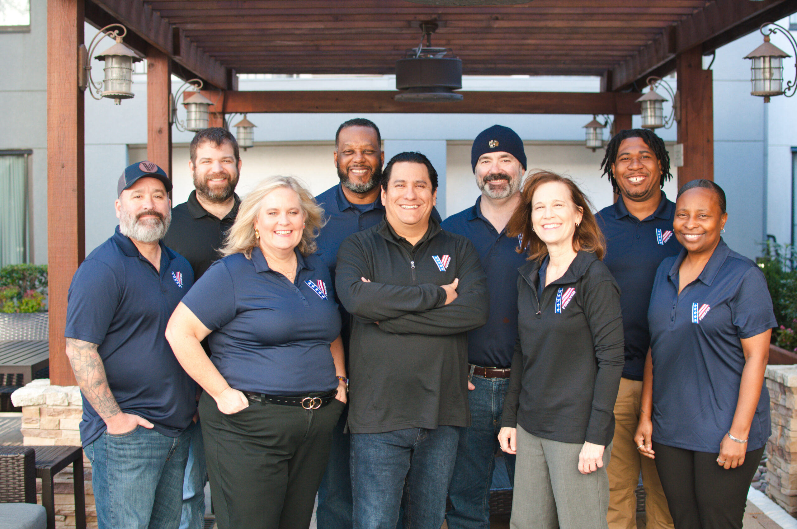 The VetsForever team standing together in branded polos under an outdoor pergola