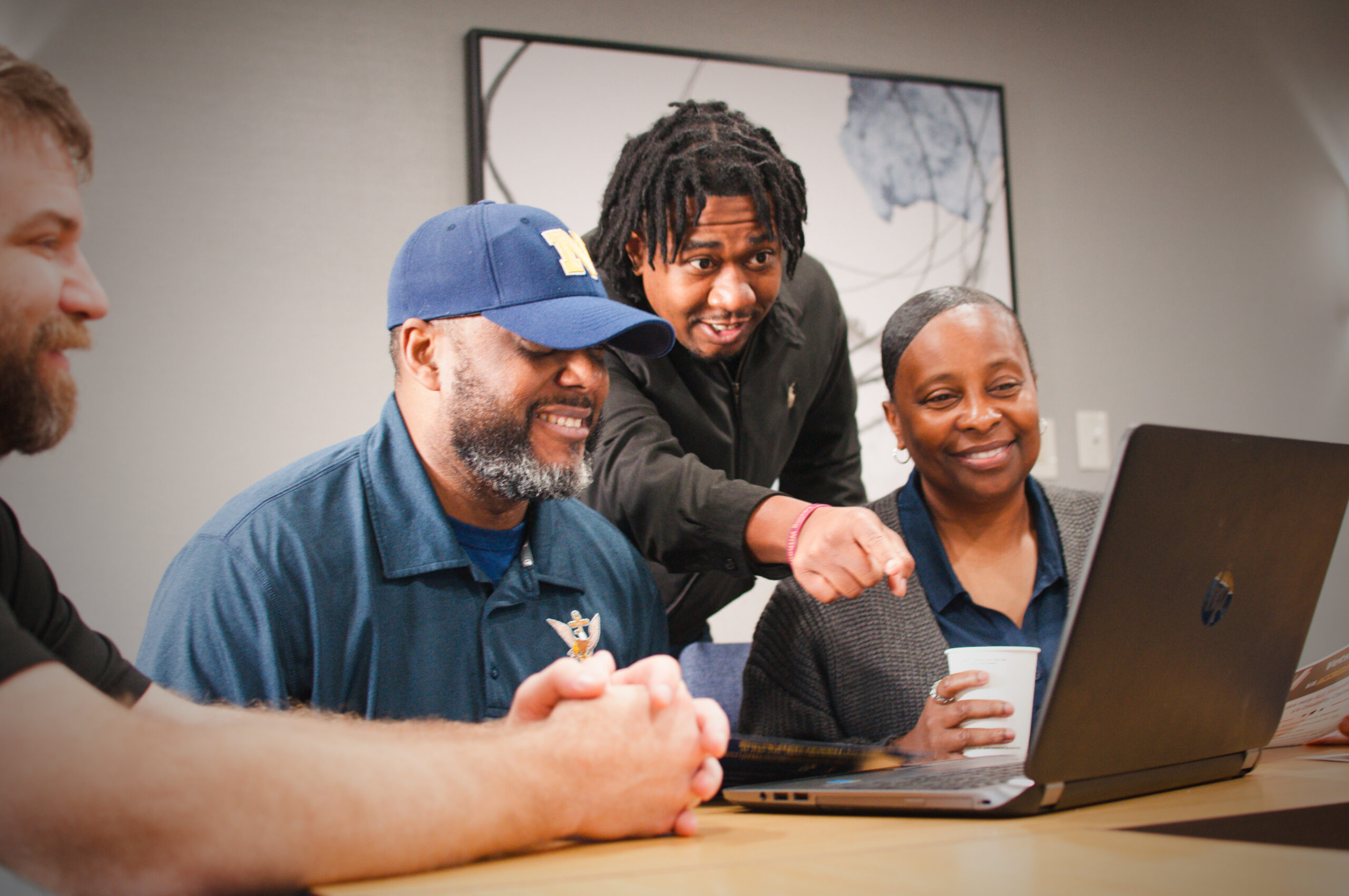 Four VetsForever team members smiling and working together at a laptop